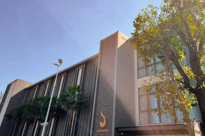 Un edificio moderno con fachada vertical, logotipo visible y un árbol en primer plano.
