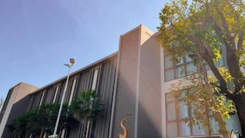 Un edificio moderno con fachada vertical, logotipo visible y un árbol en primer plano.
