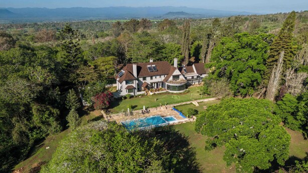 Ein großes, zweistöckiges Haus mit Schwimmbad, umgeben von dichtem Wald und Bergen im Hintergrund.