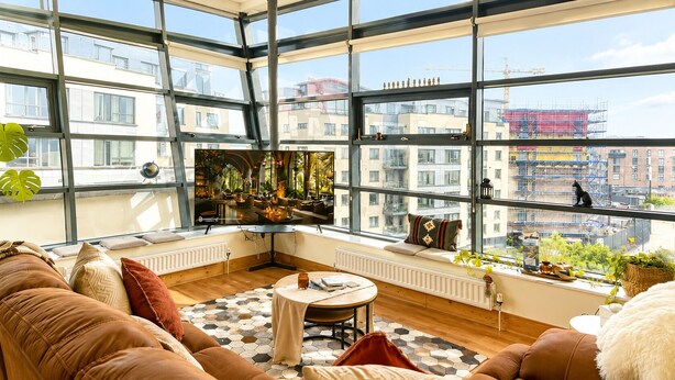 A modern living room with a large window, a sofa, a small table, and a fireplace. - Panoramic Two-bedroom Penthouse (Cork)