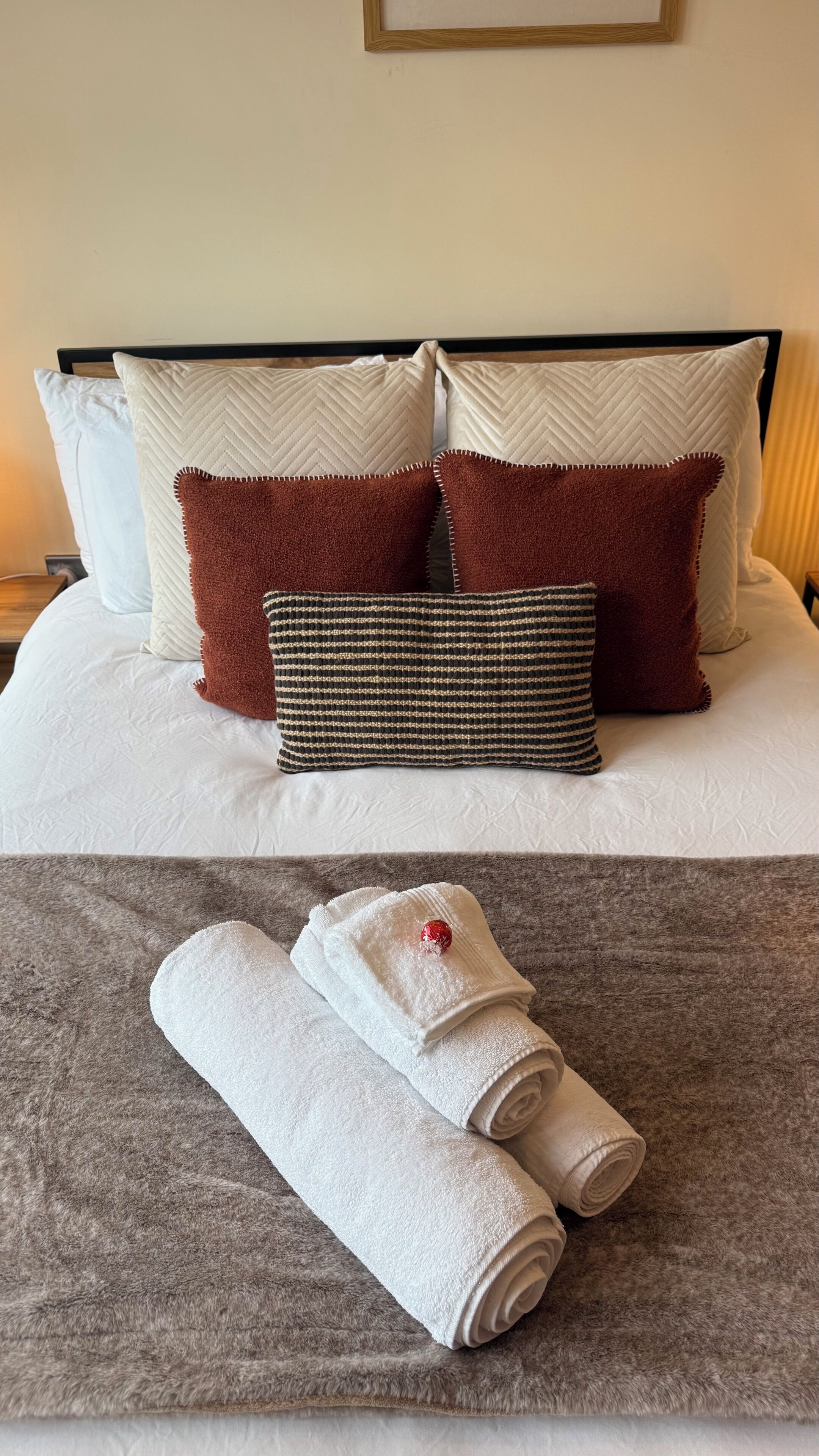 A neatly made bed with white linens, two brown pillows, and a striped pillow.
