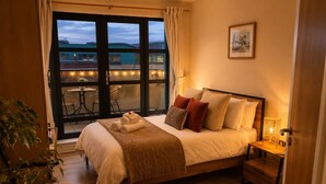 A bedroom with a bed, bedside table, lamp, and a view of the outside. - Panoramic Two-bedroom Penthouse (Cork)