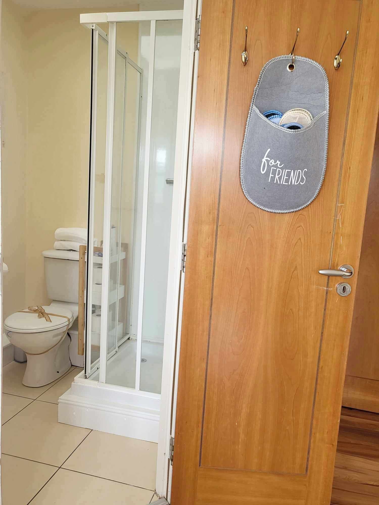 Une porte en bois ornée d’une étiquette où l’on peut lire « pour les AMIS », et une porte de douche en verre donnant accès à une salle de bain équipée de toilettes et d’un porte-serviettes.