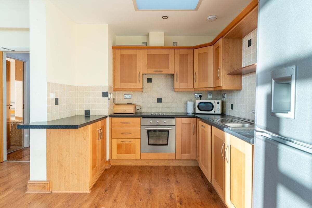 A modern kitchen with wooden cabinets, a black countertop, stainless steel appliances, and a skylight.
