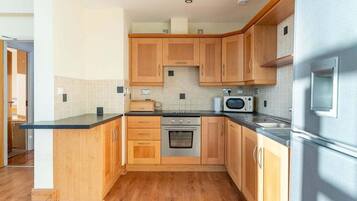 A modern kitchen with wooden cabinets, a black countertop, stainless steel appliances, and a skylight.