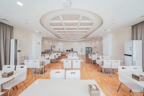 Un'ampia sala conferenze d'hotel con numerosi tavoli e sedie, una zona salotto centrale e un moderno design del soffitto.