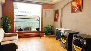 A room with a sofa, a washing machine, a dryer, and a window with a view of buildings outside. - Vienna Zhihao Hotel (Chengdu Kuanzhai Alley Zizhuhan Road East Subway Station) (Chengdu)