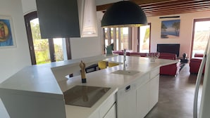 A modern kitchen with a central island, a built-in oven, and a large black pendant light. - Villa L'estancade Domaine du Douc Tourisme Dans une Ferme de la Foret des Landes (liposthey)