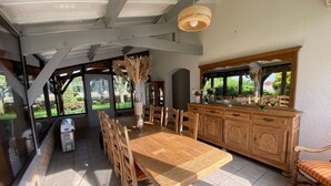 A dining area with a wooden table and chairs, a large window with a view of greenery, and a hanging light fixture. - Villa L'estancade Domaine du Douc Tourisme Dans une Ferme de la Foret des Landes (liposthey)