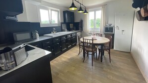 A modern kitchen with dark cabinetry, a central island, and a dining area with wooden chairs. - Jade room (Rosières)