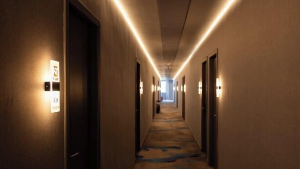 Un pasillo de hotel con apliques iluminados, suelo alfombrado y puertas a ambos lados.