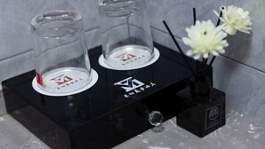 Un pedestal negro con dos recipientes de vidrio y una pequeña caja negra con un logotipo.