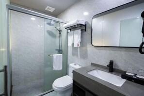 A modern bathroom with a glass-enclosed shower, a white toilet, a sink with a mirror above it, and a towel rack with folded towels.
