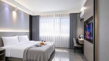 A modern hotel room with a bed, bedside table, and a desk with a chair.