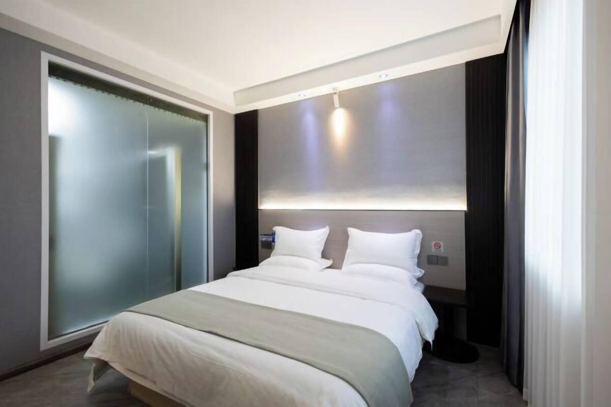 Una habitación de hotel moderna con una cama grande, un armario corredero, una lámpara fijada a la pared y una mesita de noche.