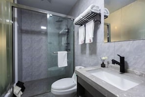 A modern bathroom with a glass-enclosed shower, a white toilet, a large sink with a black faucet, and a mirror above the sink.