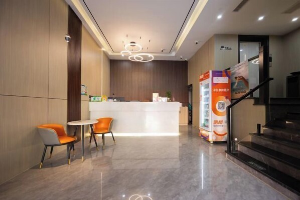 Un área de recepción moderna con un mostrador blanco, sillas naranjas y una escalera.