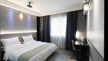 A modern hotel room with a large bed, a desk, and a window with curtains.