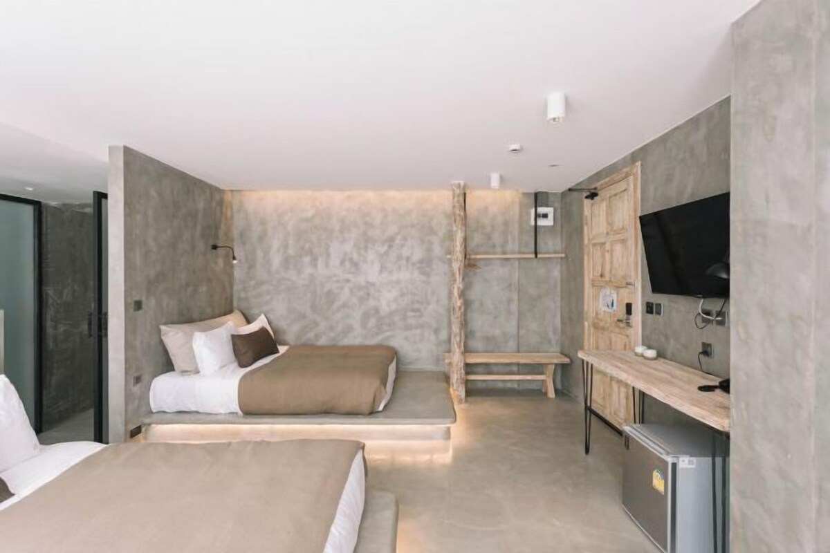 A modern hotel room with a large bed, a smaller bed, a desk with a computer, and a television.