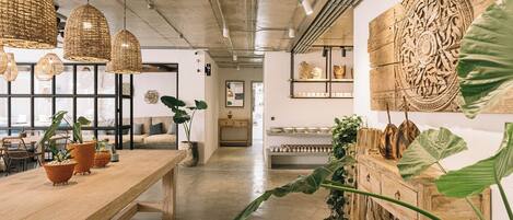Um interior moderno com uma longa mesa de madeira, luminárias de vime suspensas e grandes folhas decorativas.