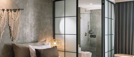 A modern bedroom with a large bed, a bedside table, a wall-mounted macrame decoration, and a glass-enclosed shower area.