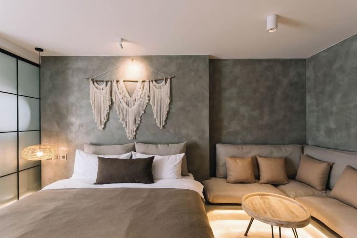 Un dormitorio moderno con una cama grande, un sofá y un tapiz de macramé en la pared.