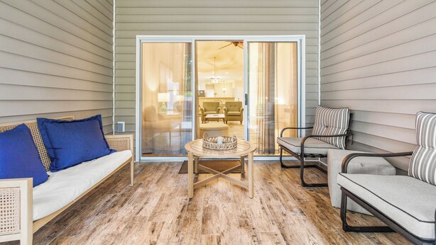 Une terrasse couverte avec un plancher en bois, une table ronde et des sièges comprenant un canapé et des fauteuils.