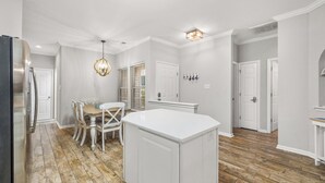 Une cuisine moderne avec des meubles blancs, un îlot central et un coin repas comprenant une table et des chaises en bois.