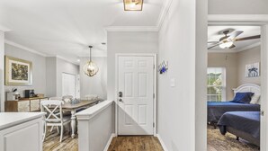 Un couloir étroit avec un plancher en bois, une porte blanche et un lit recouvert d’une couverture bleue dans la pièce adjacente.