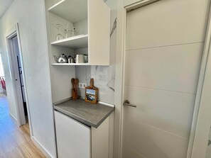 Eine kompakte Küche mit eingebautem Regal, einer kleinen Arbeitsfläche und einer Tür mit Griff.