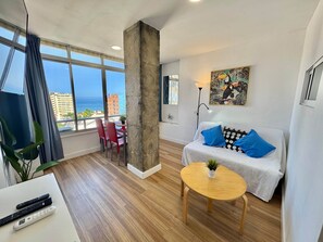 Una sala de estar moderna con un ventanal grande, un sofá con cojines estampados, una mesa de centro y un comedor con sillas.