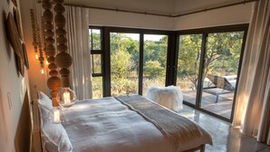 A bedroom with a large bed, a view of the outdoors through a sliding glass door, and a wooden deck outside.