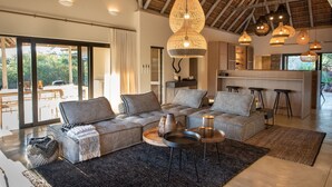 A modern living room with a large sectional sofa, a dining area, and a kitchen.