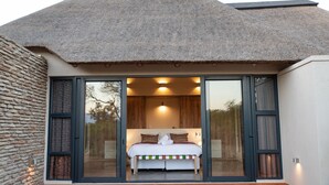 A bedroom with a large bed, sliding glass doors, and a thatched roof. - Villa Scarabee: Wonderful luxury villa in the middle of nature (Hoedspruit)
