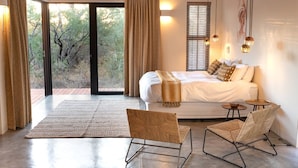 A modern bedroom with a large bed, a view of trees through the window, and a balcony. - Villa Scarabee: Wonderful luxury villa in the middle of nature (Hoedspruit)