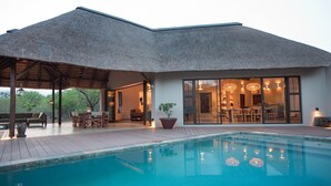 Una casa moderna con piscina, mobiliario exterior y un patio cubierto.