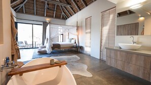 A modern bedroom with a large bed, a canopy, a bathroom with a freestanding bathtub, and a large window. - Meet Villa Safari: a 5-star exclusive villa (Hoedspruit)