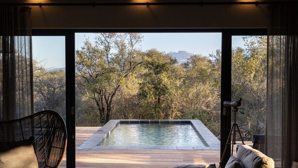 A pool with a wooden deck and a view of trees and mountains. - Meet Villa Safari: a 5-star exclusive villa (Hoedspruit)