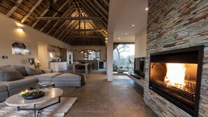 A modern living room with a stone fireplace, a dining area, and a kitchen. - Meet Villa Safari: a 5-star exclusive villa (Hoedspruit)