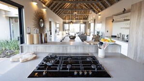 A modern kitchen with a central island, a gas stove, and a dining area with a sofa and table. - Meet Villa Safari: a 5-star exclusive villa (Hoedspruit)