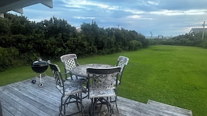 A covered outdoor patio with a wooden deck, a round table, four chairs, and a grill. - Historic Harkers Island Bungalow (Harkers Island)