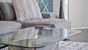 Un soggiorno moderno con un tavolino in vetro, un divano grigio e una coperta a righe.