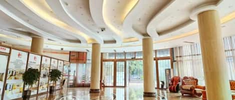 A spacious lobby with a polished marble floor, large columns, and a modern ceiling design.