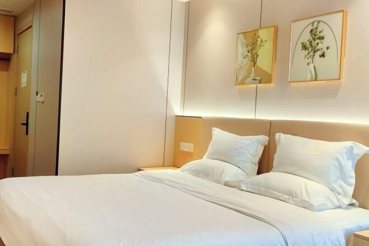 A neatly made bed with white linens, a wooden headboard, and two framed botanical prints on the wall.