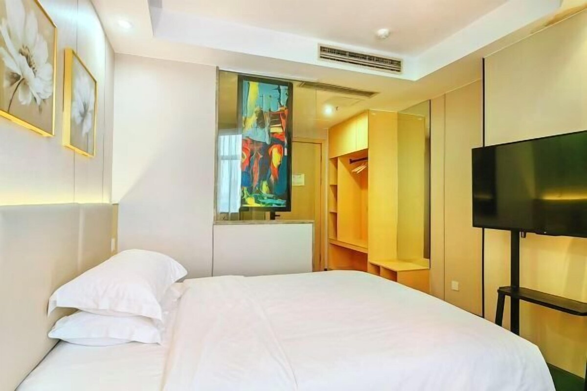 A hotel room with a bed, a TV, a wardrobe, and a painting on the wall.