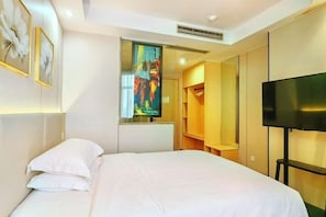 A hotel room with a bed, a TV, a wardrobe, and a painting on the wall.
