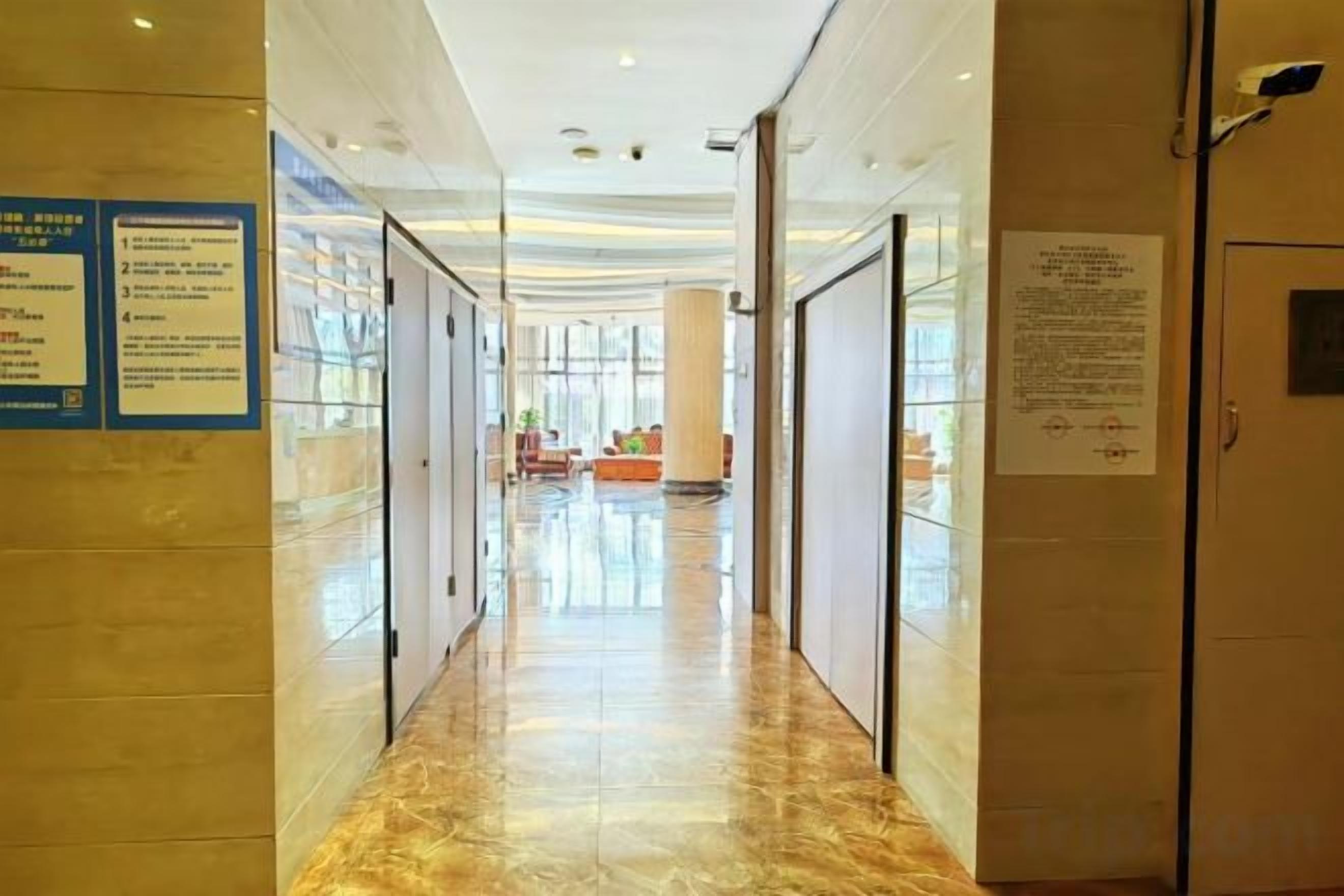 Un pasillo de hotel con puertas de cristal, suelo de mármol y señalización informativa.
