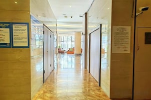 A hotel corridor with glass doors, a marble floor, and informational signs.