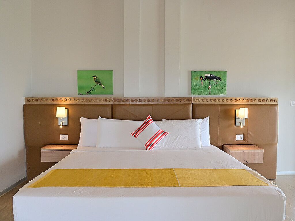 A hotel room with a large bed, two wall-mounted lamps, and two framed pictures on the wall.