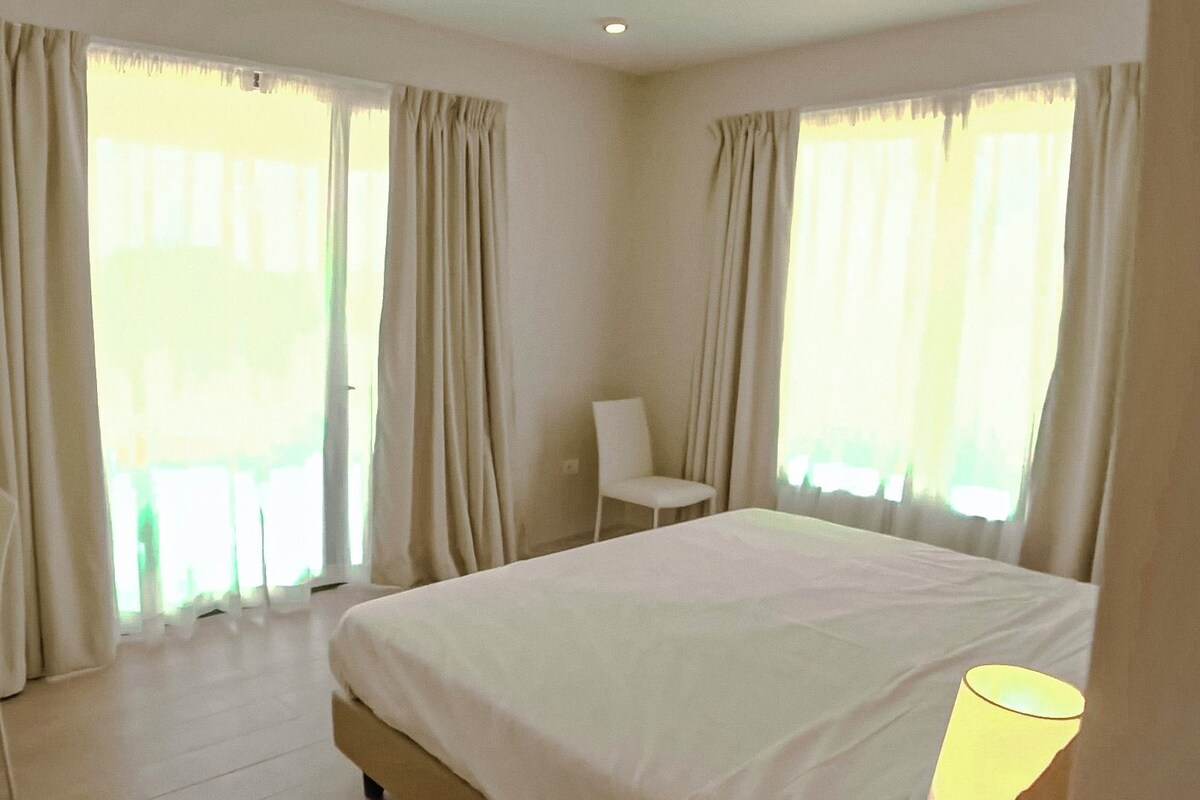 A hotel room with a large bed, a chair, and two windows with curtains.